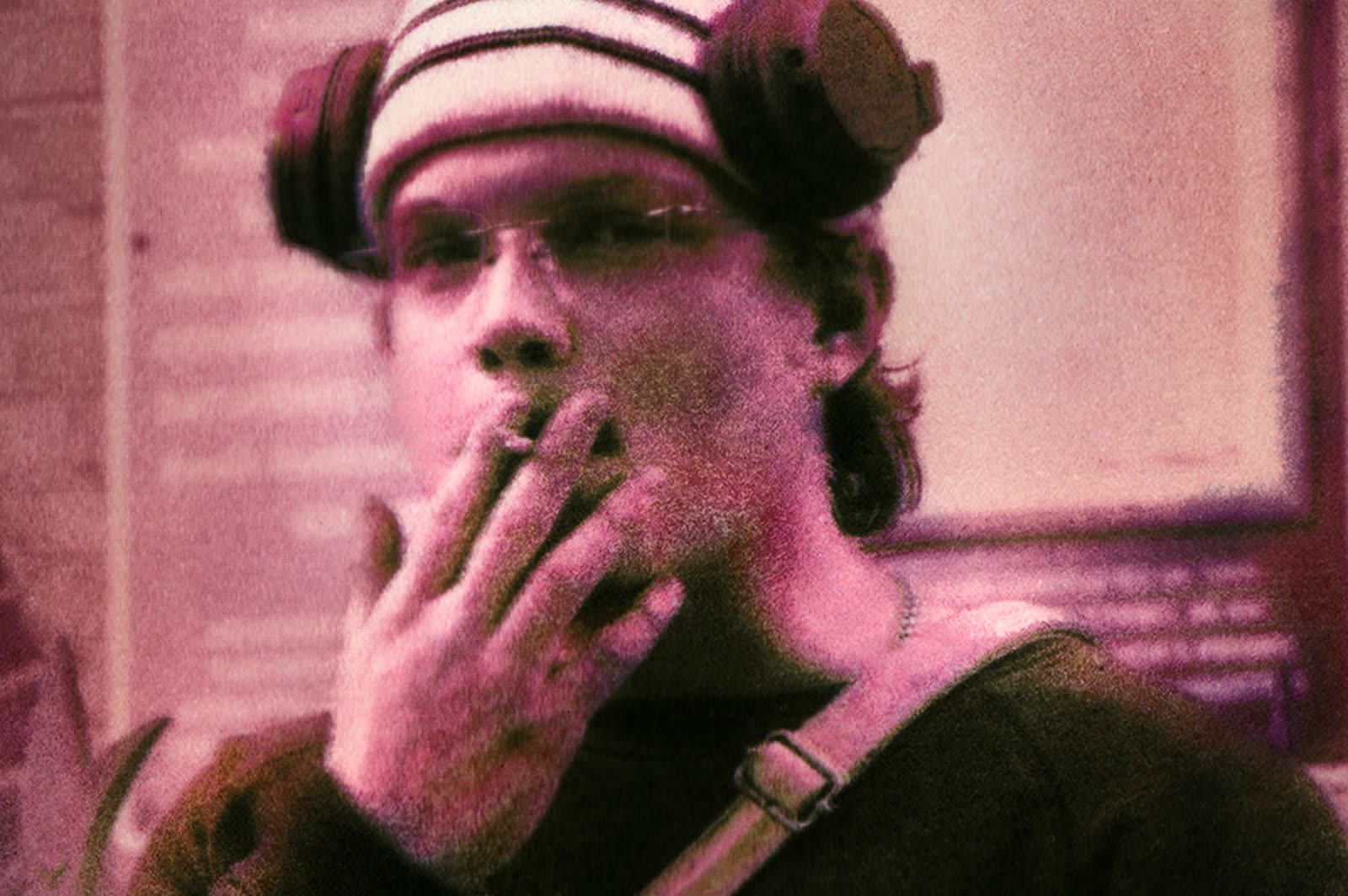 Magenta-lit portrait, hand raised to the face.
