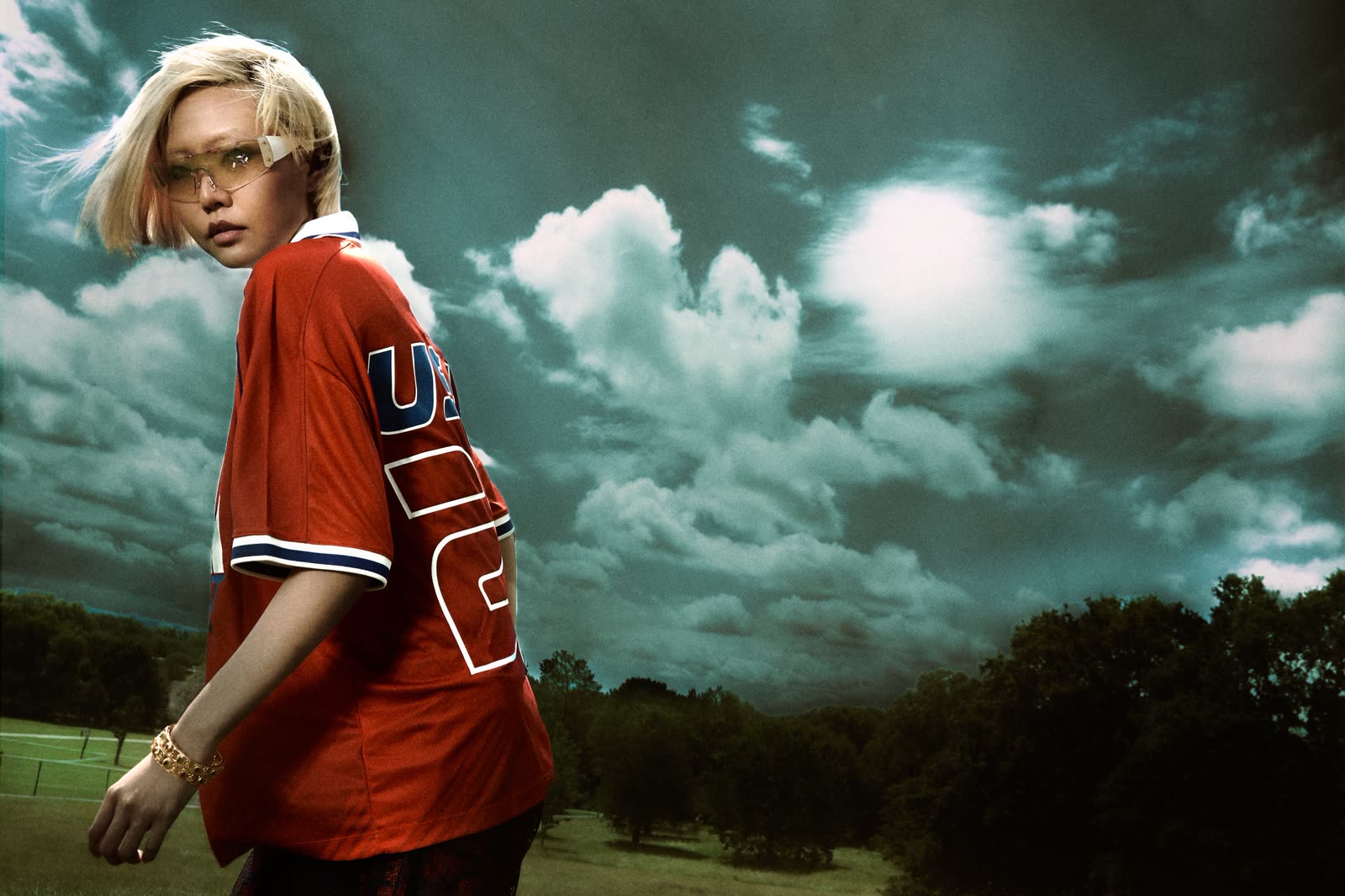 Figure in a red jersey beneath a heavy cloudscape.